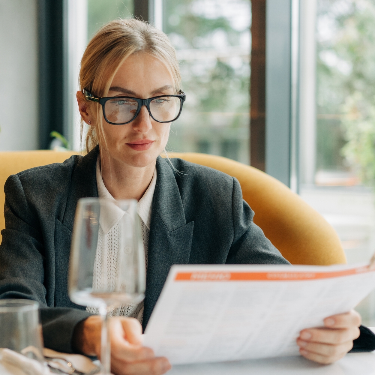 A chic woman in a tailored dark blazer and collared shirt reading a menu in a restaurant, showcasing French girl style and executive wear for petites.